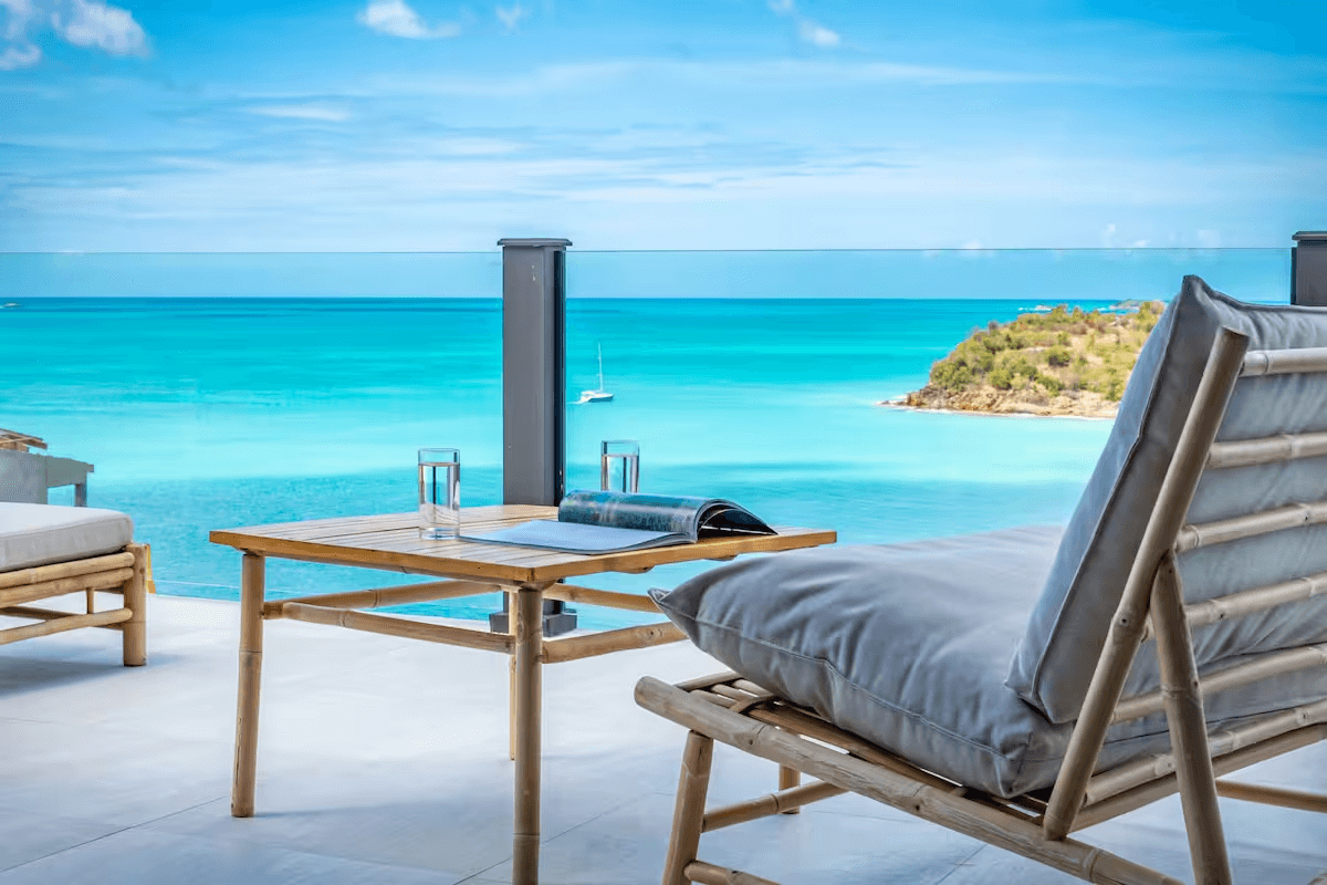 An outdoor balcony at Tamarind Hills Resort and Villas - Antigua, with a lounge chair and a table overlooking the sea.