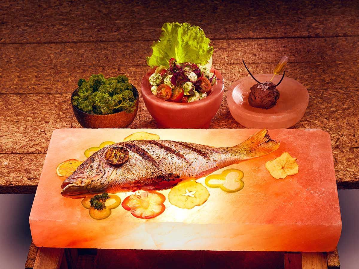 Grilled fish served with fresh vegetables and a side salad on a wooden platter