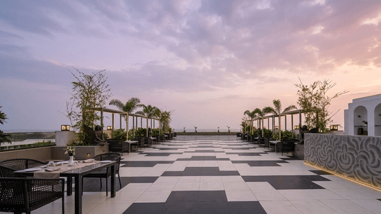 A clifftop ceremony space with two rows of chairs facing a small altar area, shaded by a wooden pergola with a cloudy sky overhead.