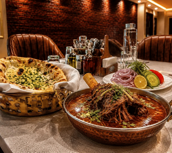 Dining table at Lime Tree Hotel & Banquet, Jaipur, with a bowl of meat curry, a basket of naan and a side salad.