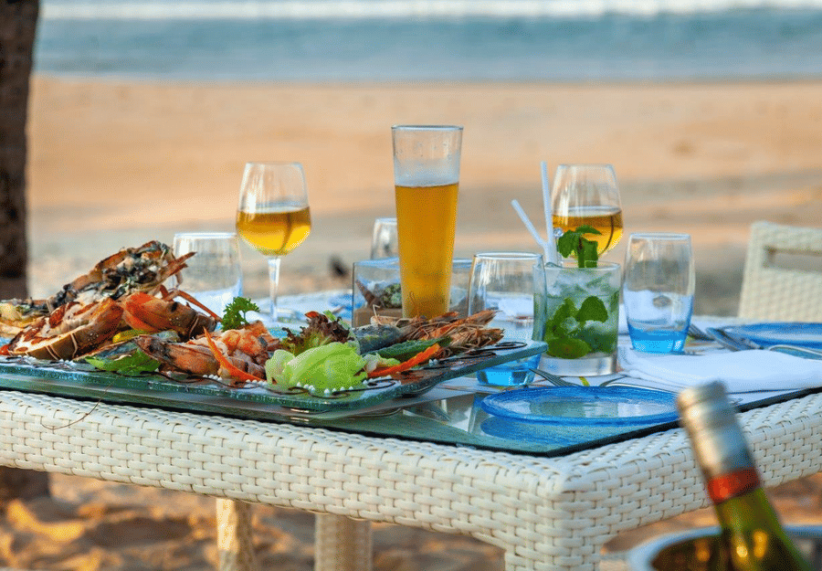 a close up shot of a table with many food items and beverages by the beach - Caravela Beach Resort Goa