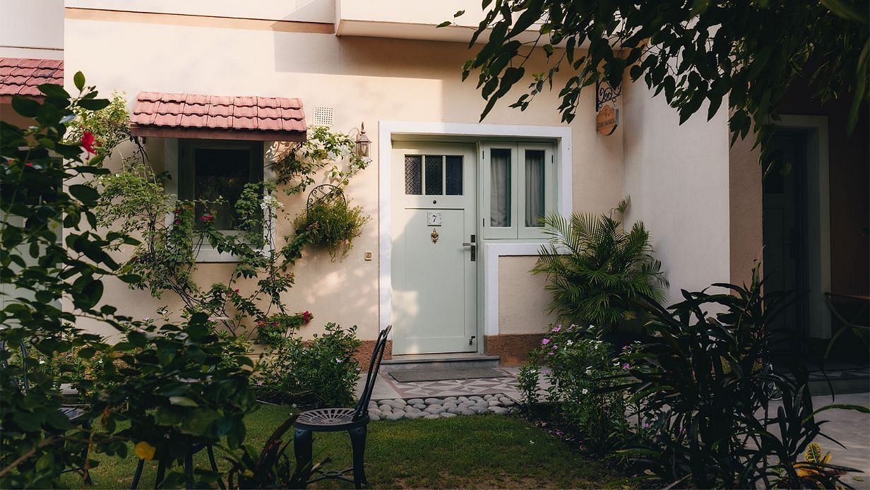 Front entrance of a cream-coloured house with a red awning and plants in the garden at Karma Chalets.