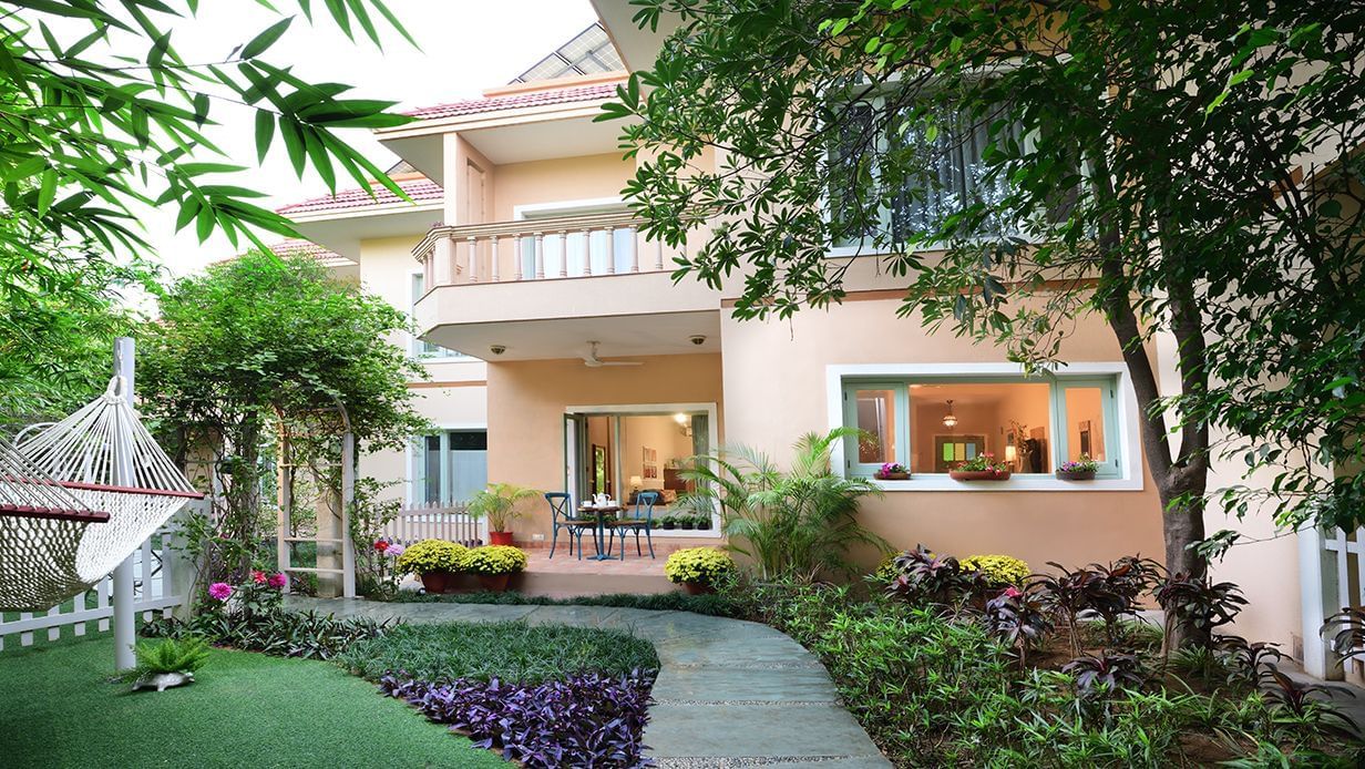 Villa garden with stone pathway, hammock, flowering plants, and outdoor seating in front of a peach-colored house at Karma Chalets.