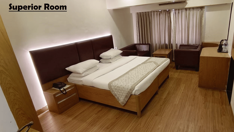A Superior Room at Kings International Juhu with a bed, a flat screen TV facing the bed, a nightstand and an A/C unit.