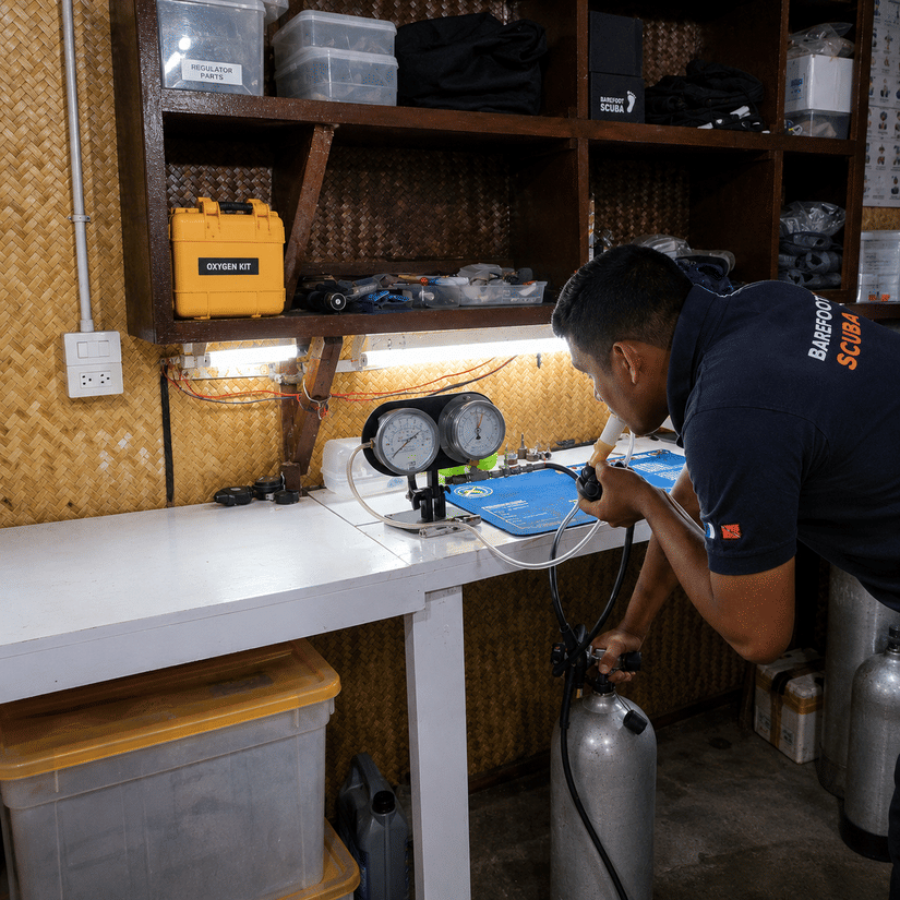 A dive professional checking and servicing scuba diving equipment at a workshop.