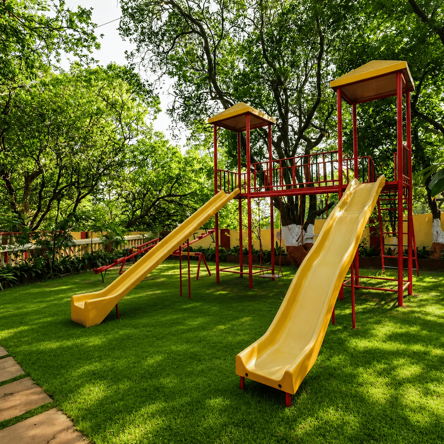 A kids' play area with two slides and two see-saw surrounded by trees.
