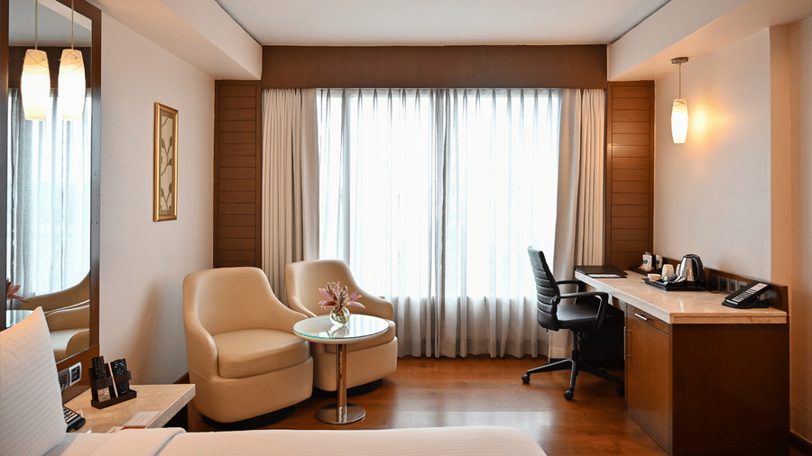 A spacious hotel suite featuring a seating area, desk, and large windows, offering a comfortable stay.