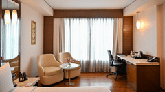 A spacious hotel suite featuring a seating area, desk, and large windows, offering a comfortable stay.