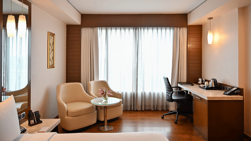 A spacious hotel suite featuring a seating area, desk, and large windows, offering a comfortable stay.