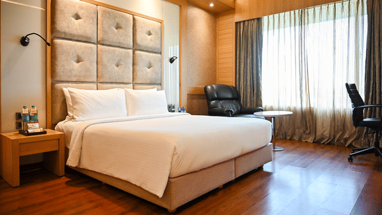 A well-appointed hotel room with a large bed, wooden headboard, and elegant furnishings, suggesting comfort and luxury.