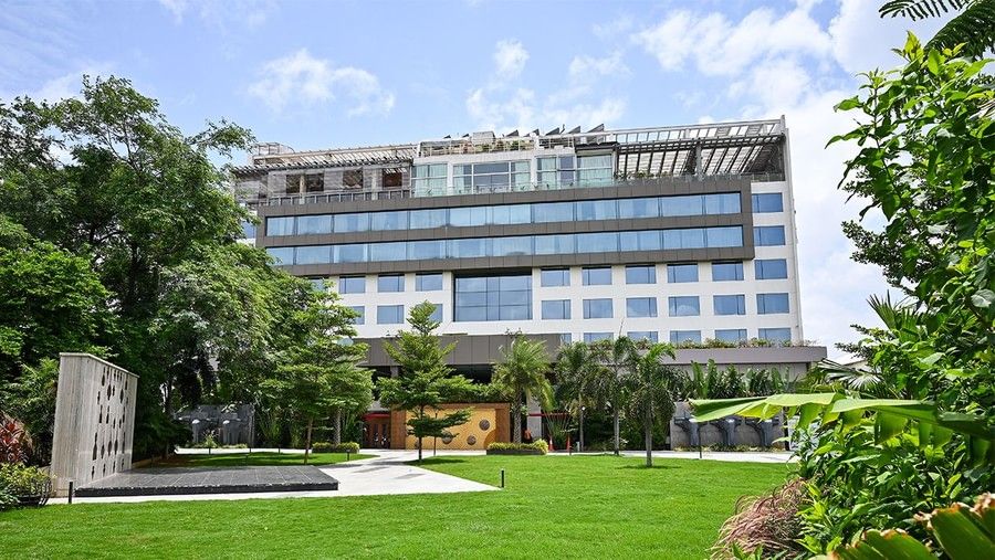 The exterior of Hotel Daspalla, a modern building surrounded by lush green lawns and trees under a blue sky.
