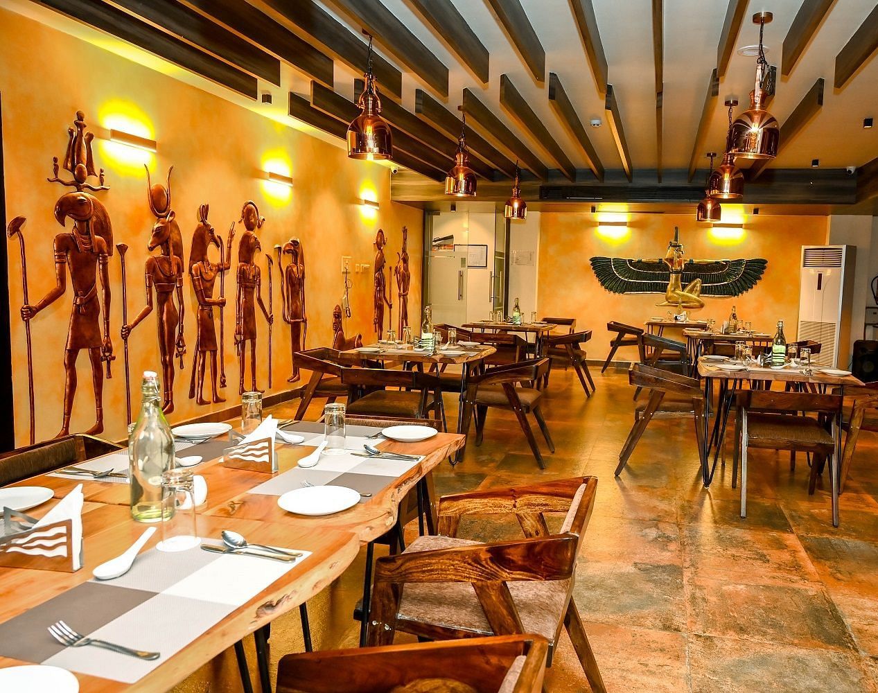 A side view of the restaurant dining area, showcasing set tables, the wooden ceiling, and the collection of decorative statues lining the walls - Sea Hills Hotels, Sri Vijaya Puram (Port Blair)