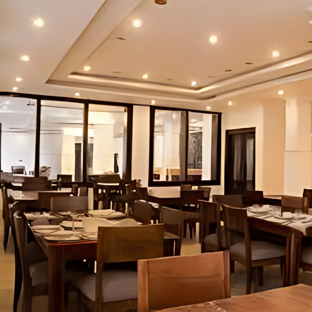 The spacious indoor restaurant at Hotel Dekiling by Eastlynn Collections, Leh, with wooden dining sets, pillars, and large glass windows.