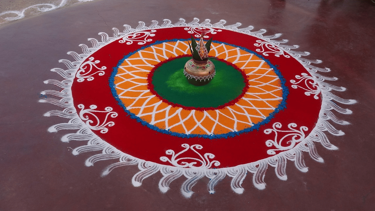A circular rangoli on the floor featuring vibrant coloured patterns with a kalasha at the centre.