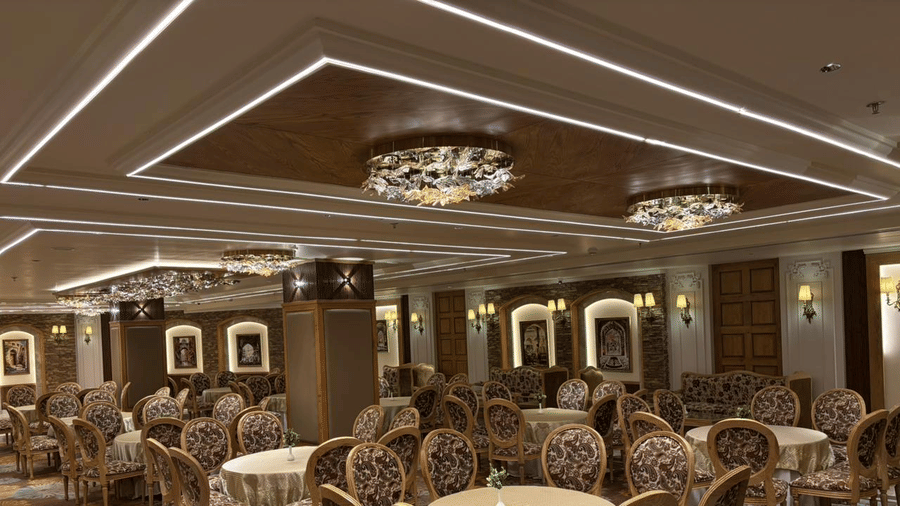 Dining setup in the banquet hall of Presidium Sarovar Premiere, Dalhousie with chairs and circular tables.