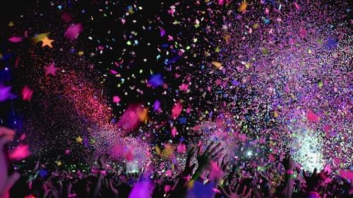 Crowd celebrating with colourful confetti falling during a music event.