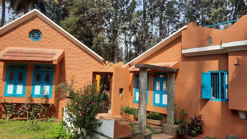 Orange cottage-style rooms with blue window frames at Casa Cottage - Heritage Hotel in Bangalore, set amongst green gardens and tall trees
