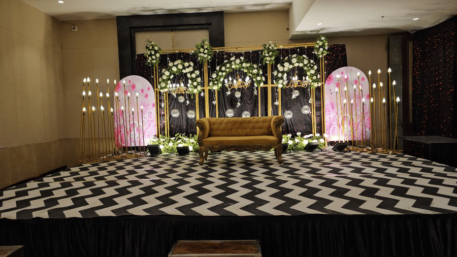 A wedding stage with floral backdrop, candles, and sofa seating in a banquet hall at Ambrosia Sarovar Portico, Haridwar.