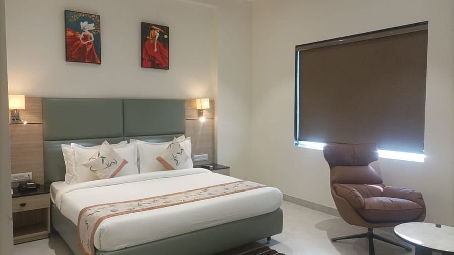 A well-lit deluxe room in Clarks Inn Express, Firozabad, with a neatly made king size bed and a lounge chair.