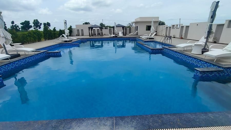Rooftop swimming pool with tiled edges, surrounded by lounge chairs and closed umbrellas; cabanas and a building structure are visible in the background, with greenery and a cloudy sky beyond the pool area - Kyriad Prestige, Ilkal