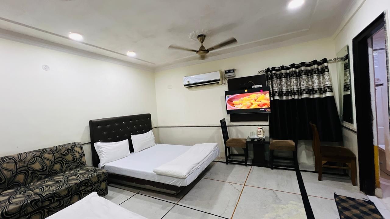 A family room at Ajay Guest House featuring two beds, a comfortable sofa, and a television, perfect for a relaxing stay.
