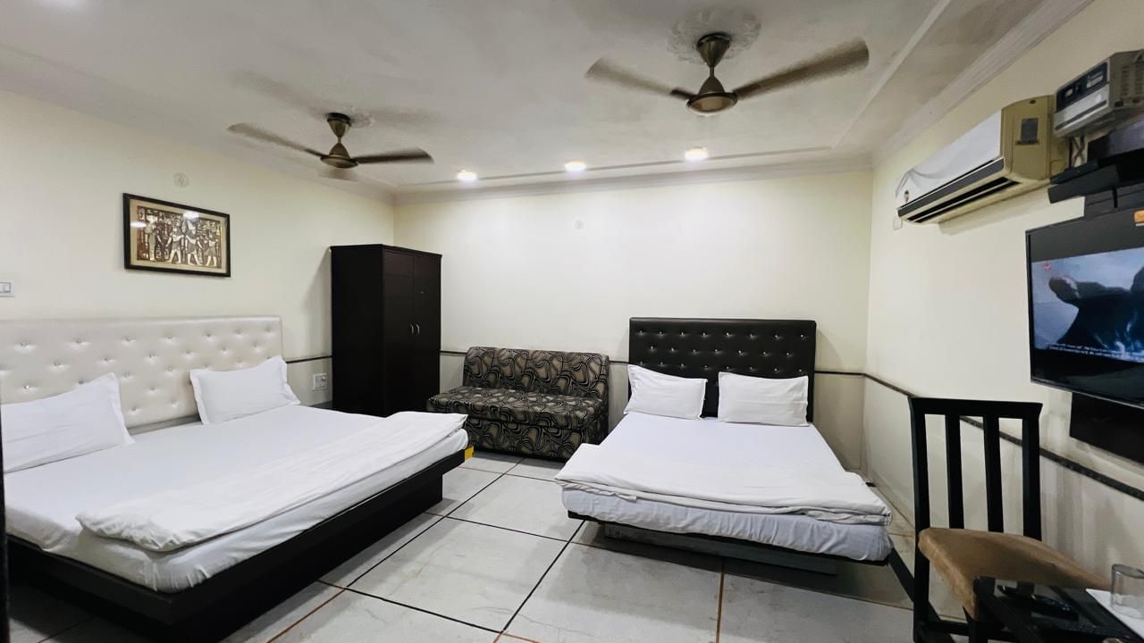 A family room at Ajay Guest House with two beds, a sofa, and a television, providing a functional and inviting space for families.