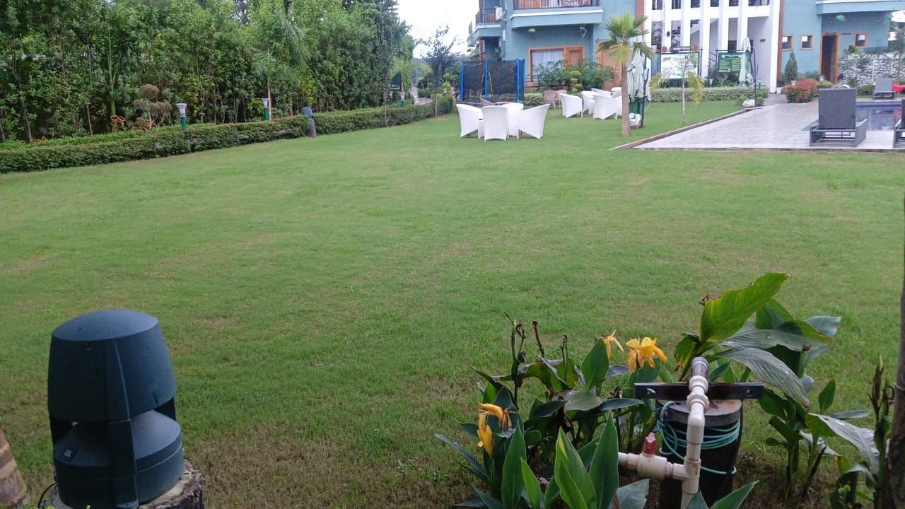 Full view of the lush green lawn area with several white coloured chairs kept at a distance at Corbett Nirvana Resort.