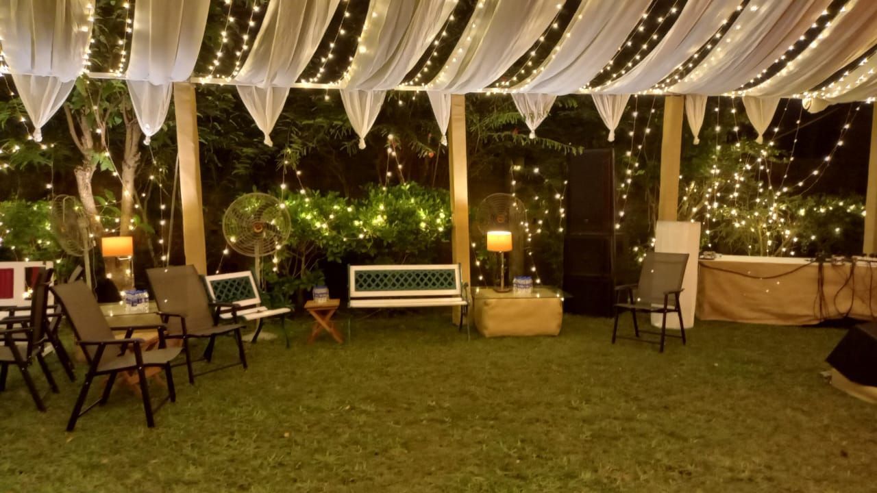 A beautifully decorated outdoor event space at night, featuring draped white fabric, string lights, and seating arrangements on a grassy lawn