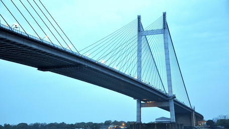 Large suspension bridge spanning over a calm river with boats underneath at twilight.