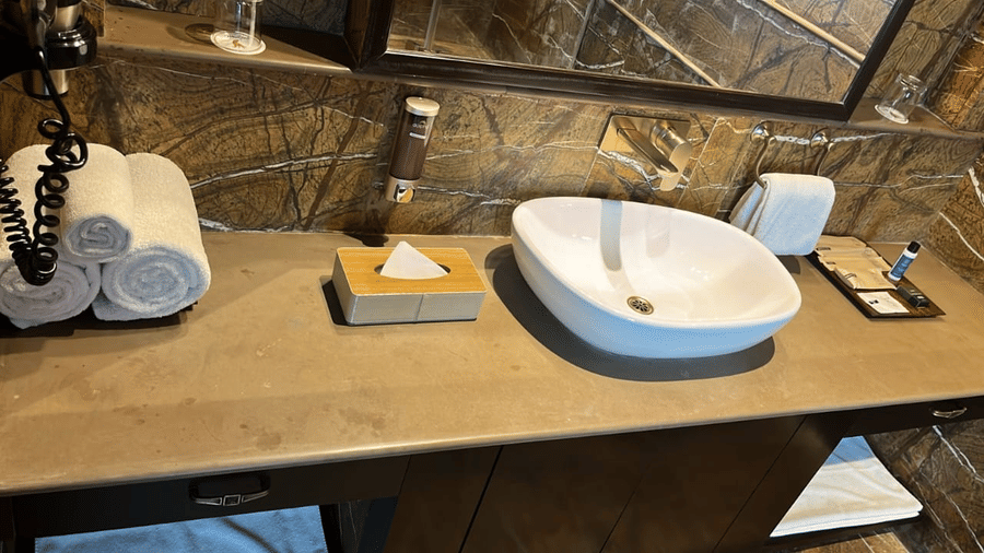 A modern bathroom vanity with a basin, toiletries, and fresh towels at Aamaghati Wildlife Resort.
