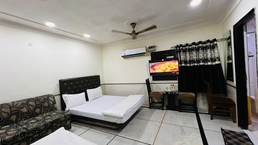 A family room at Ajay Guest House featuring two beds, a comfortable sofa, and a television, perfect for a relaxing stay.