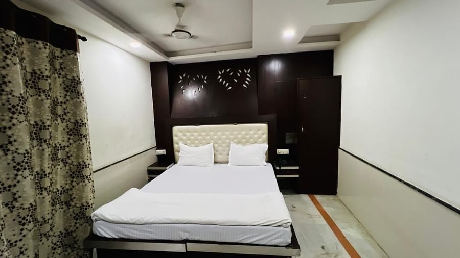 A well-appointed deluxe room with a bed and dark wooden furniture, creating a warm and inviting ambiance for guests. | Deluxe Room | Ajay Guest House