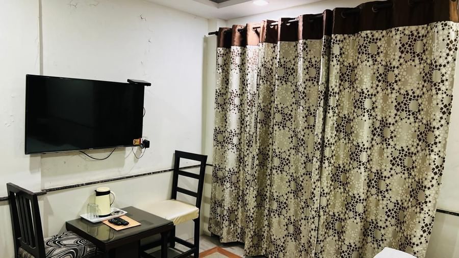A simple deluxe room with a TV mounted on the wall and a small table, providing essential amenities for a comfortable stay. | Deluxe Room | Ajay Guest House
