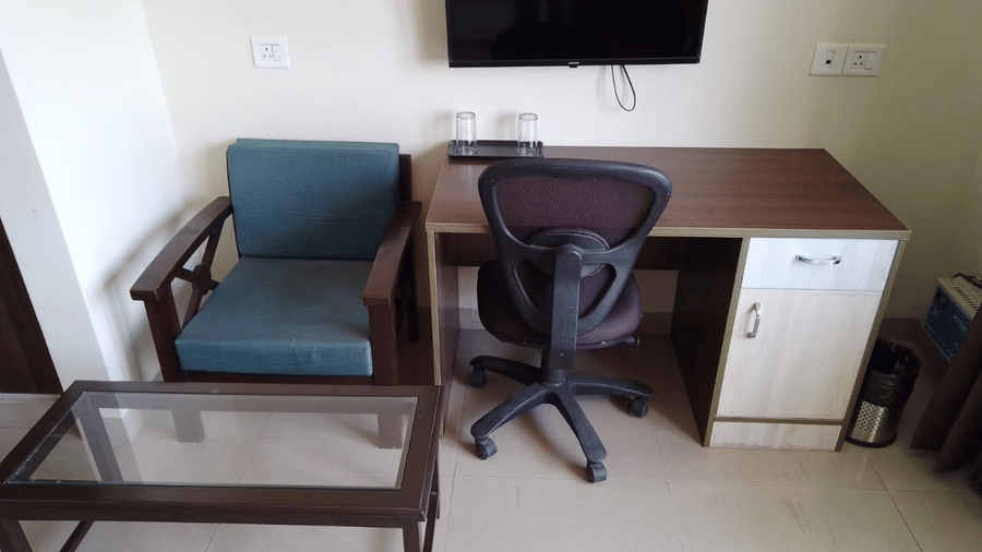 Work desk setup with office chair, a wooden chair, glass-topped table and TV at Livbox, Rudrapur.