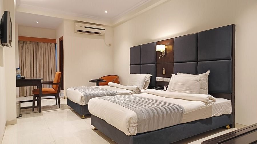 A hotel bedroom with two single beds, dark headboards, and a seating area - Lords Eco Inn Dahej