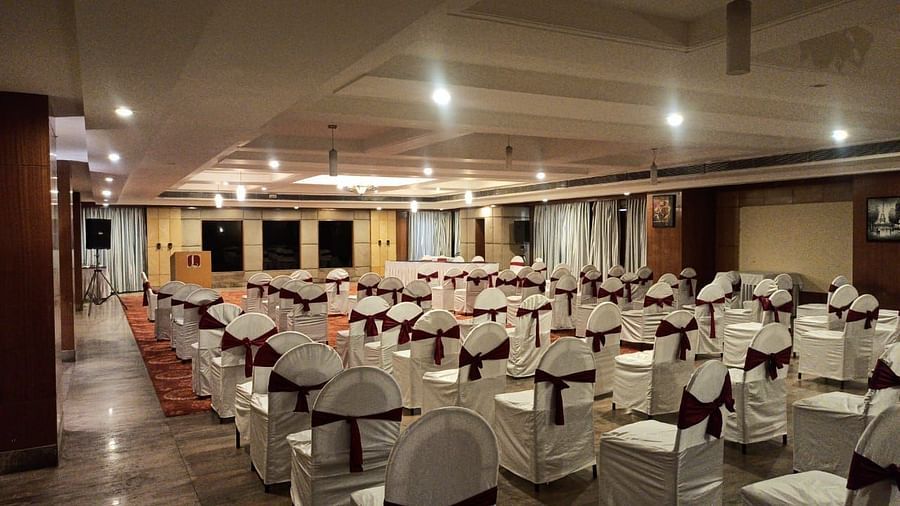 A large banquet hall with rows of chairs arranged, bright ceiling lights, and a clean, neat setup - Lords Plaza Ankleshwar