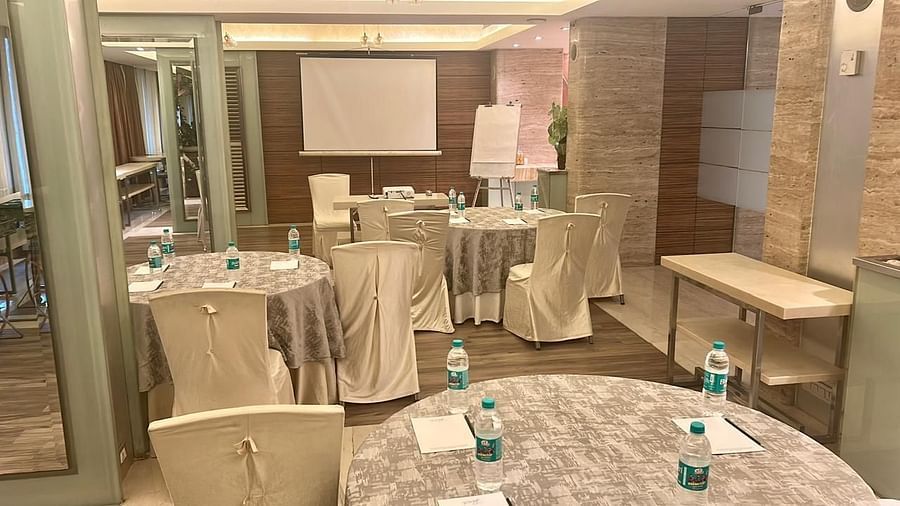 Round tables with tablecloths and white chairs in a brightly lit function hall, arranged for a social event or reception at Mirage Hotel, Mumbai.
