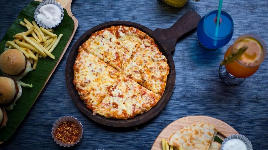 Top view of a table with various fast foods like pizza, fries, burgers, and dips, along with two drinks placed at Oriental Aster, Mumbai.