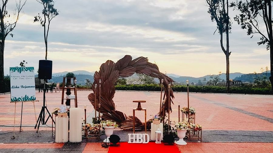 An outdoor wedding venue is set up with a floral arch and red carpet, with a scenic view in the background | Open Deck | Woodstock Resorts, Coorg