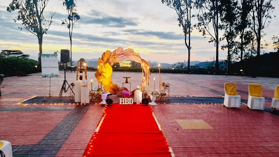 An outdoor wedding setup features a red carpet leading to a floral archway, with chairs arranged on either side and greenery in the background | Open Deck | Woodstock Resorts, Coorg
