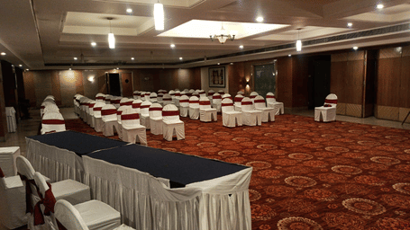 Large banquet hall of Lords Plaza Ankleshwar featuring neatly arranged chairs, a carpeted floor, and modern interiors