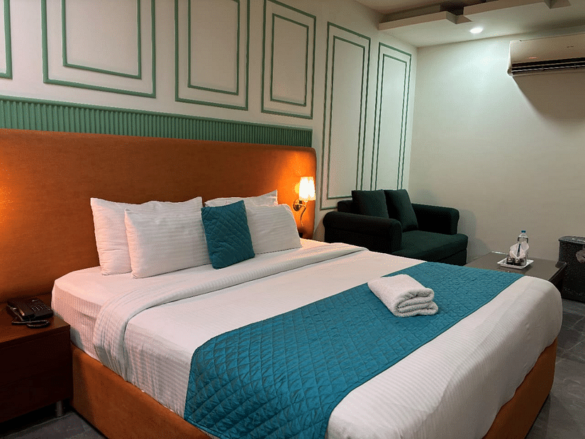 An interior view of a hotel room featuring a bed with pillows,  a sofa and decorative wall paneling - Asian Suites IFFCO Chowk Metro Station, Gurgaon. 