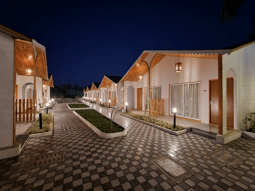 A view of the cobbled walkway with manicured lawn in the centre and Cottages on either side, as seen during the night at VITS Daman Devka Beach, the hotel provides the best accommodation in Daman.