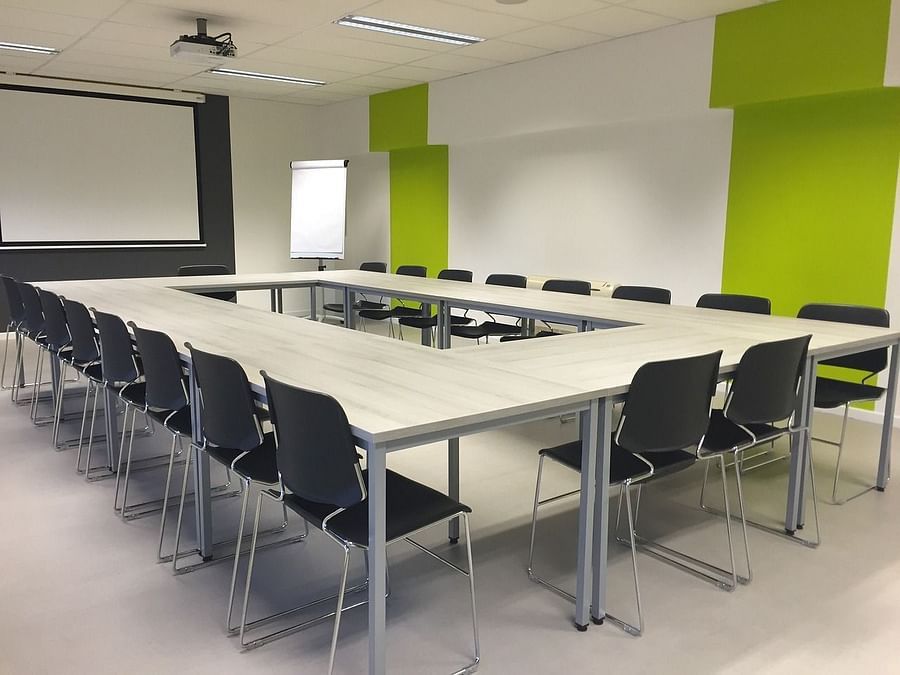 A seating area with multiple chairs a big table and a projector