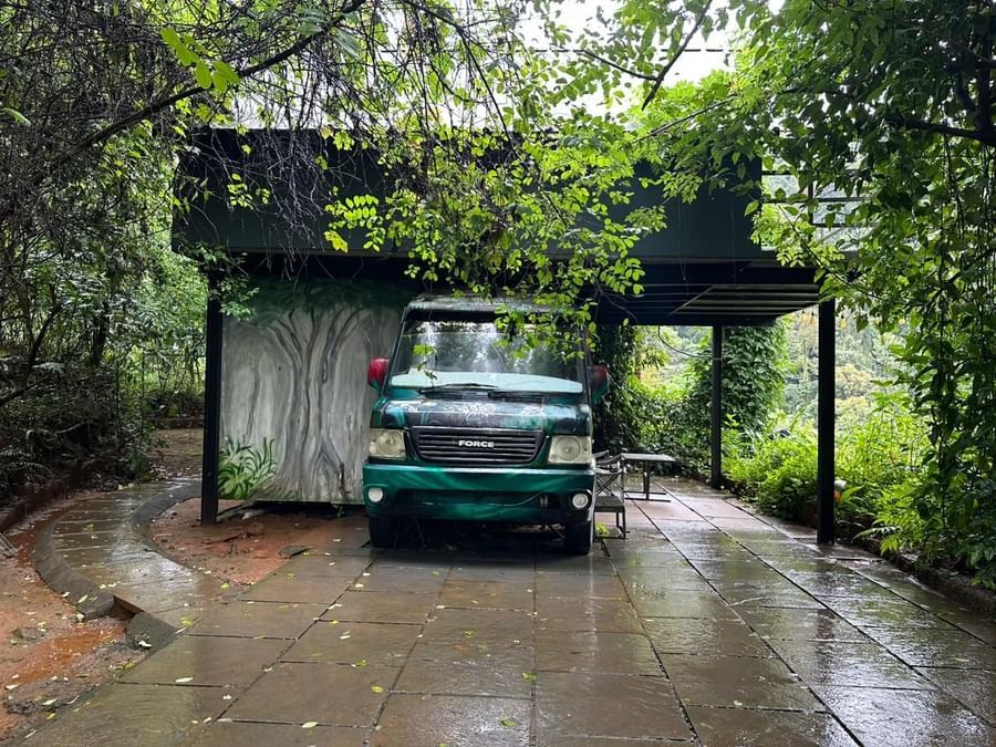 Natural stone driveway with classic green vehicle surrounded by lush rainforest vegetation at Holistic Eco-Resort, Kannur Retry