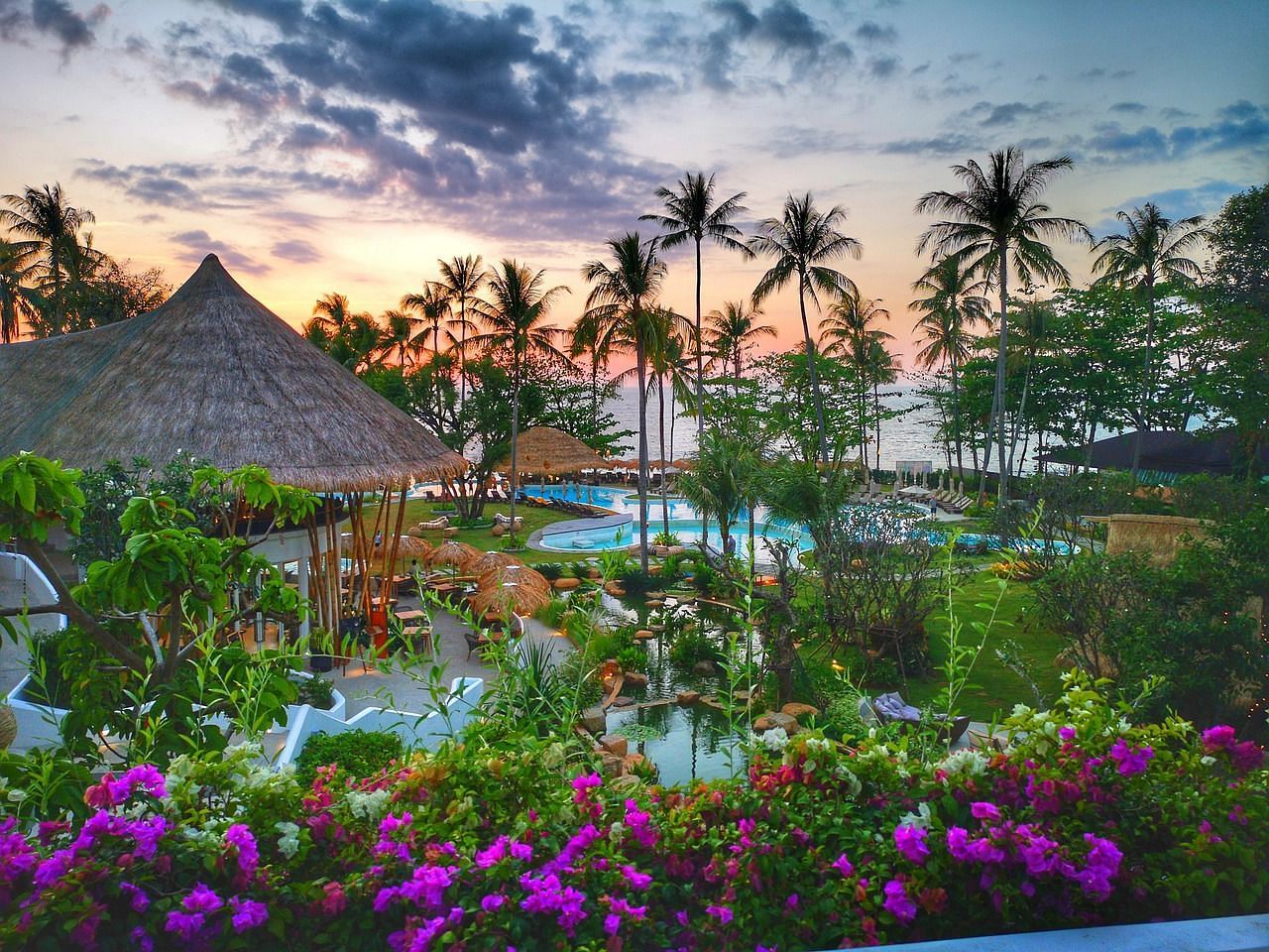 Tropical resort at sunset with lush vegetation and thatched-roof structures.