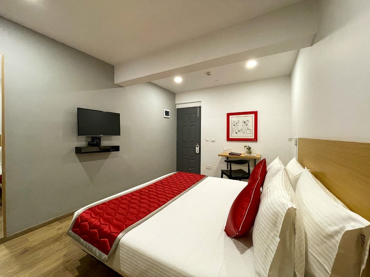 A bedroom featuring a double bed featuring a red and white bed runner along with a wall mounted television on the wall - Lords Eco Inn Belagavi