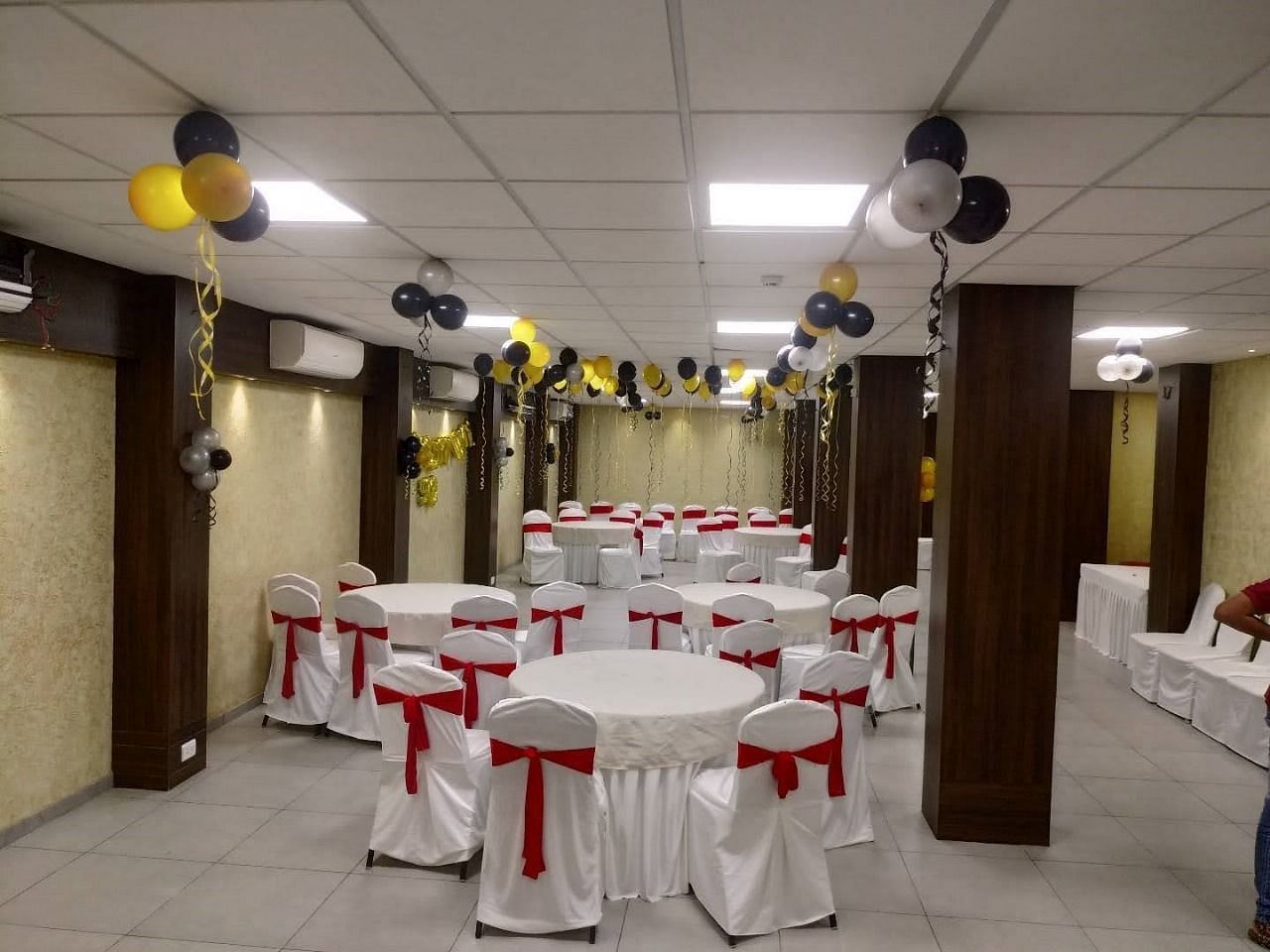 A banquet hall with tables covered in white cloths and red accents and balloons - Lords Hotels & Resorts