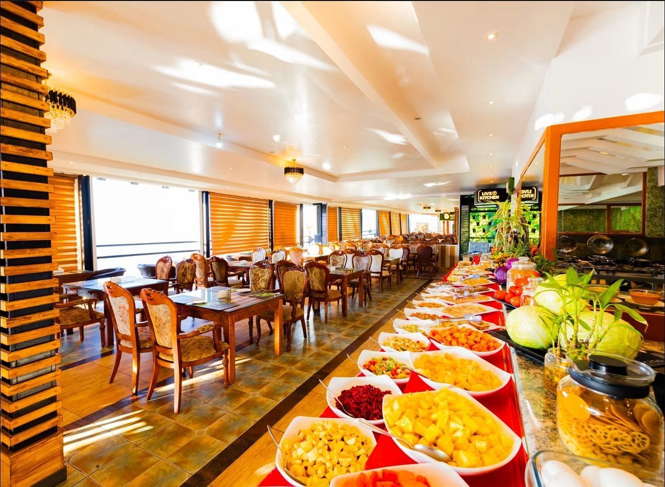 An image of a dining area where there's a buffet served at one side and a seating arrangements made with chairs and tables on another side - Parakkat hotel & resorts