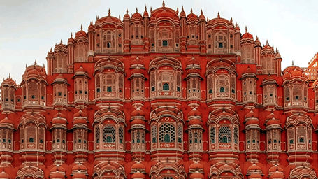 The iconic red and pink sandstone facade of the Hawa Mahal featuring intricate latticed windows and domes in Jaipur.